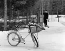 Lantbrevbärare, postiljon Erik Bergman (cykelåkande) i
Delsbo.  April 1956.

Brevbäringsturen är 2 ½ mil lång och omfattar nästan 300 hushåll. Postväskan väger ofta 30-40 kg.