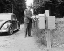 Bilkåkande lantbrevbäraren Cyril Falk på linjen Lönsboda-Hunshult-Björkhult-Lönsboda. Vid brevlådesamling i Hunshult, Blekingegränsen. Foton maj 1961.