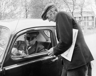 Postkunden Anton Olofsson i Rumpeboda får dagens post av bilkåkande lantbrevbäraren Cyril Falk på linjen Lönsboda-Hunshult-Björkhult-Lönsboda.  
Foto maj 1961.