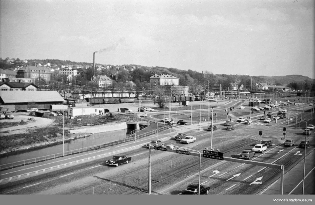 Mölndals nedre med spårvagnsspår, bilväg, järnväg och kulverteringen av Mölndalsån, innan motorvägen och bron byggdes. Skorstenen står på Papyrus-området. Utsikt från Folkets hus mot sydost, 1960-tal.