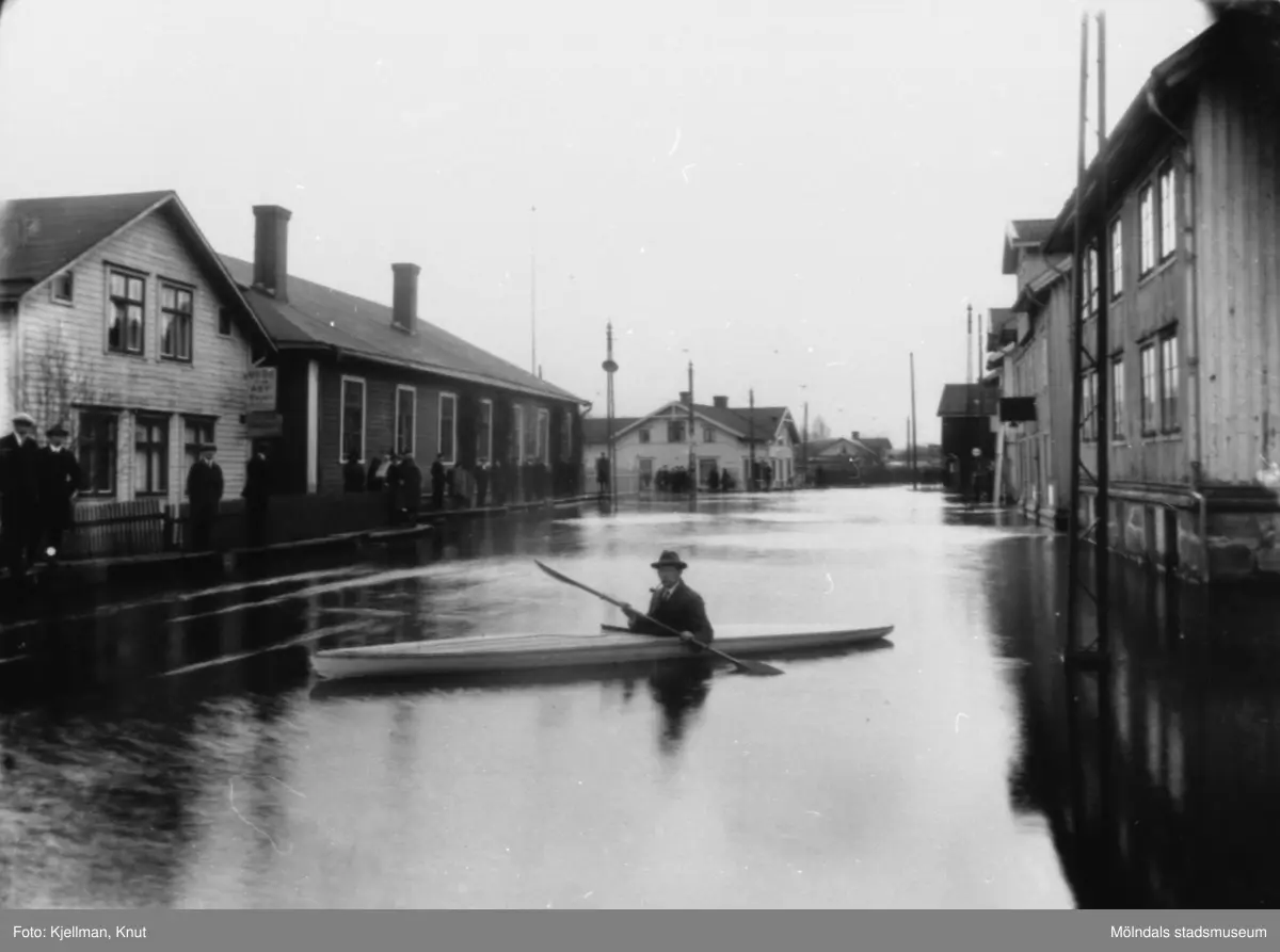 Översvämning vid Mölndalsbro, 1930-tal. Gösta Viktorinus paddlar omkring i kanot. Från vänster ses skomakare Gustaf Adolf Petterssons fastighet, spårvagnshallarna, bankhuset (Kungsbackavägen 1), Stibergs (Kungsbackavägen 2) samt Göteborgsvägen 1, 3 och 5.