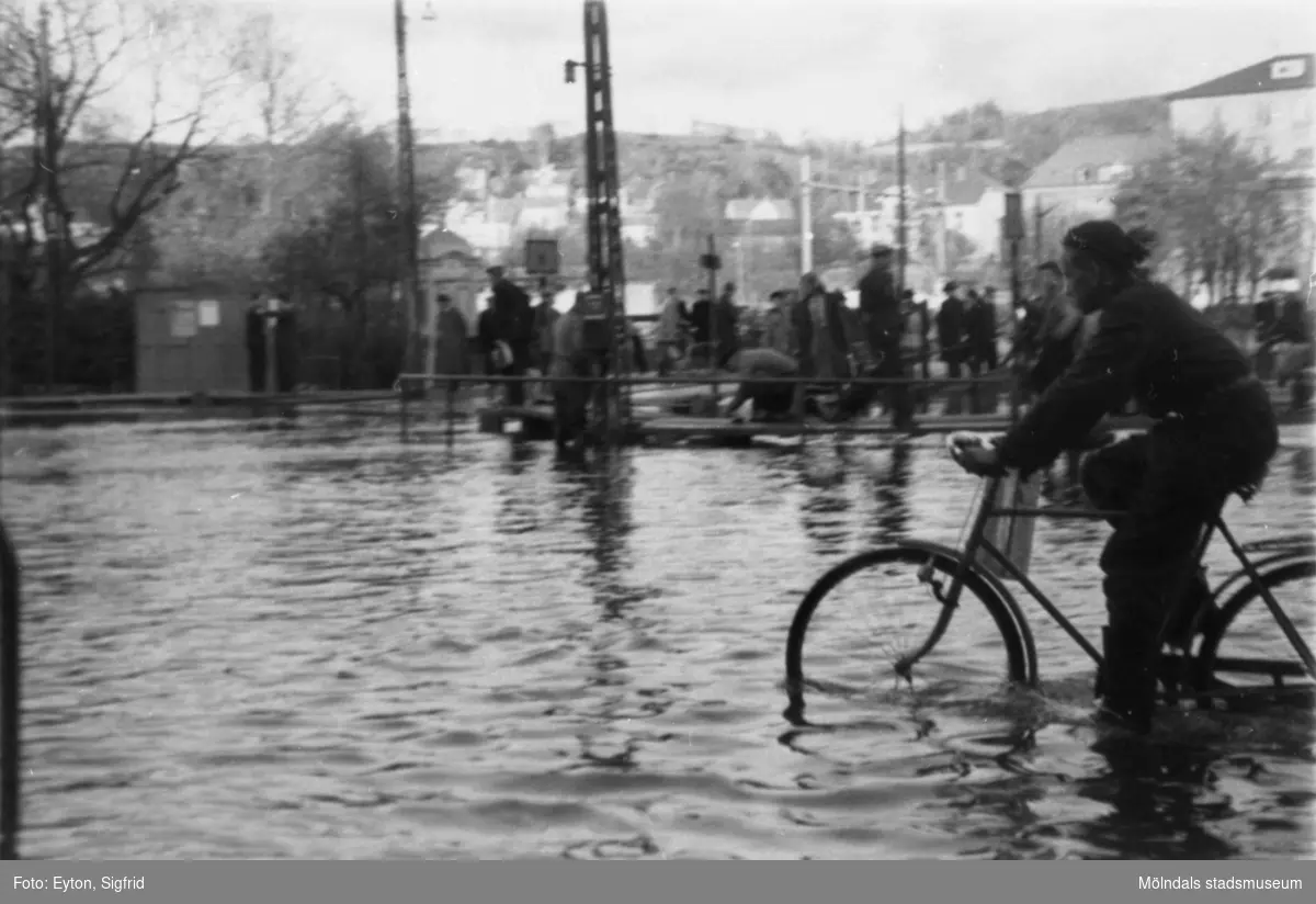 Vy mot öster, korsningen Kvarnbygatan-Frölundagatan samt Göteborgsvägen-Kungsbackavägen som är översvämmad 1951. 
I bakgrunden ses bron över ån, Kvarnbyskolan och 
biografen Röda kvarn (Kvarnbygatan 1).