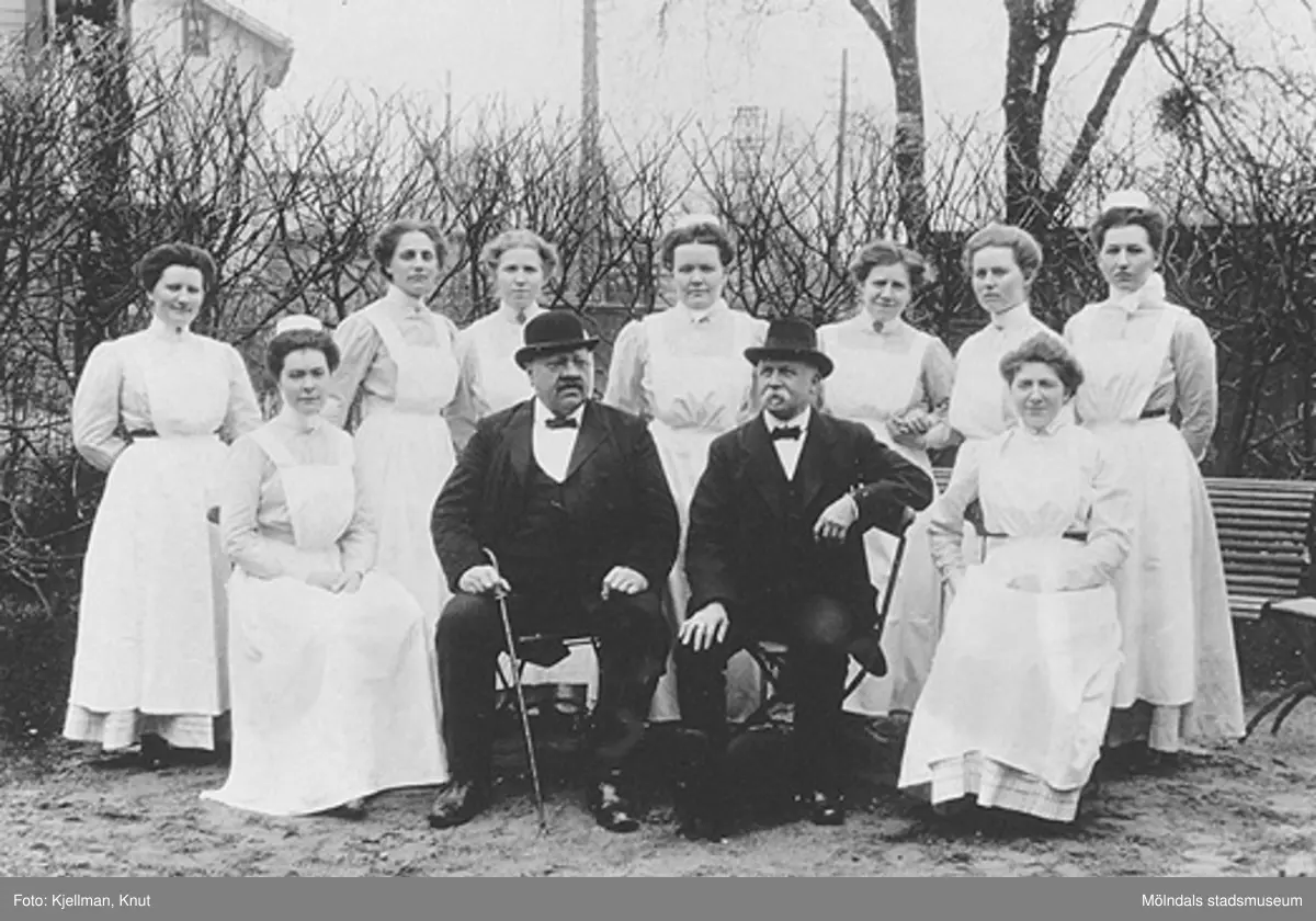 Under bilden står: "Minne af Mölndals Sjukstugas 25-årsjubileum den 30 april 1911". 
Man ser doktor Knut Belfrage, sysslomannen och sjuksköterskorna. Dessutom står de uppradade personernas namn och i förekommande fall även titlar, uppräknade. På baksidan av kartongen står: "Mölndals sjukhus den 30 april 1911, vid dess 25-årsjubileum". Kortet finns också registrerat på bild nr. MMF 92:110.