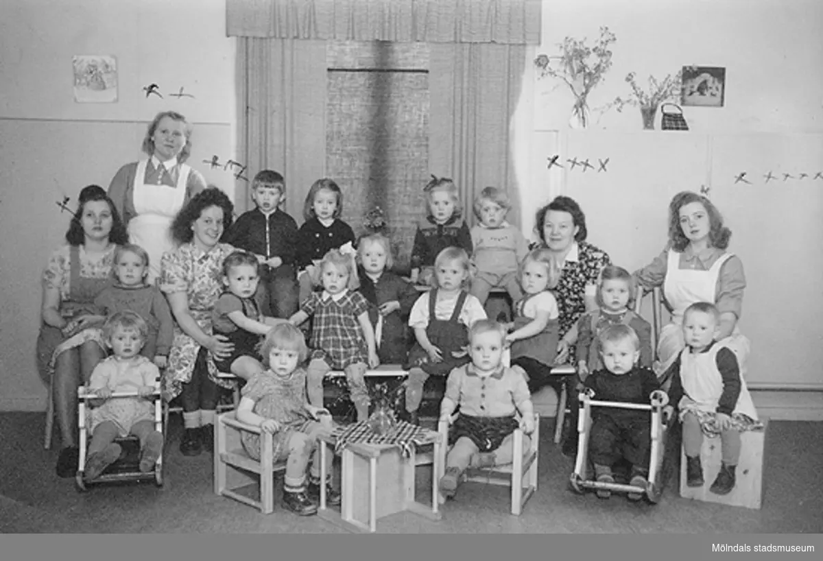 Gruppfoto av barn med förskollärare och praktikanter, bl.a "praktikant" Margit, en praktikant från Norge och ett biträde anställt från Mölnlycke Fabriker.
Kortet sitter i Margit Wannerbergs fotoalbum.