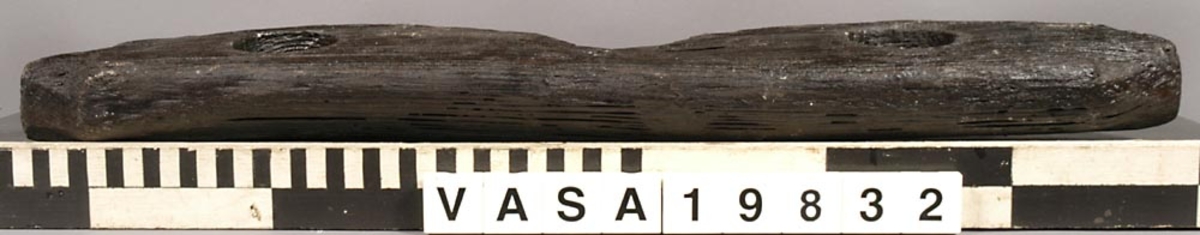 Racksläde.
Långsmal form, rak längs ena sidan och vågig på den andra. Tre genomgående hål, varav två större mot ändarna och ett mindre mot mitten.
Har en ev. förslitning ovanför båda stora hålen, som extra breda fasade kanter.