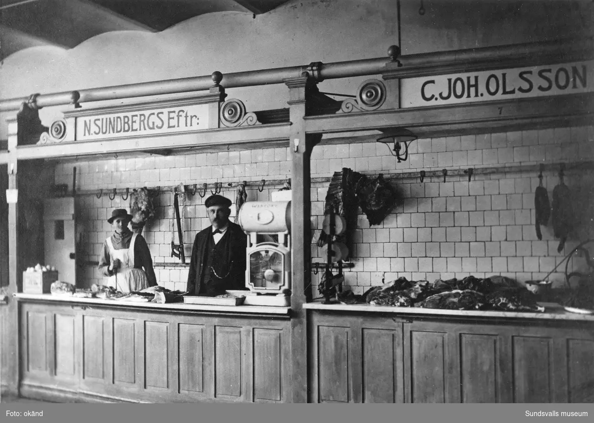 Köttbutik i Saluhallen i Holmströmska huset 1913. Carl Johan Olsson (45 år) med hustrun Olga (34 år). N. Sundbergs efterträdare. Paret var bosatt på Byggmästaregatan, Södermalm.