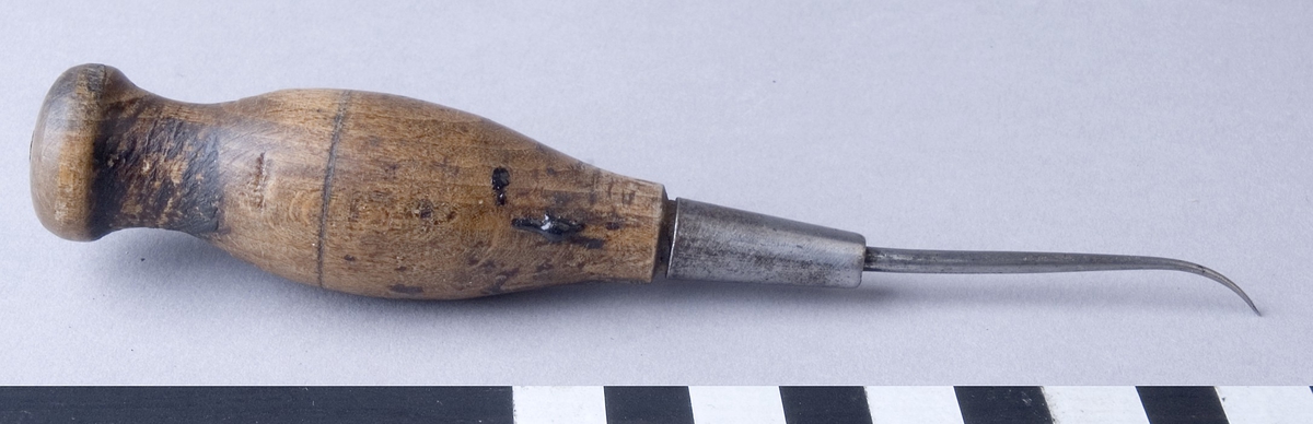 Syl, flatsyl, fabriksgjord av stål, med svarvat handtag av trä. Sylen är fäst i handtaget med hjälp av en metallhylsa och är böjd framtill med slipat platt skär.
Märkt otydligt: "..SS...ON"