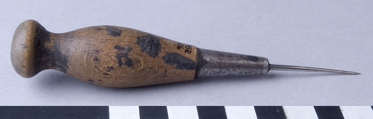 Syl, sticksyl, fabriksgjord av stål med svarvat handtag av trä. Sylen är fäst i handtaget med hjälp av en metallhylsa.
Handtaget har några fläckar av beck.