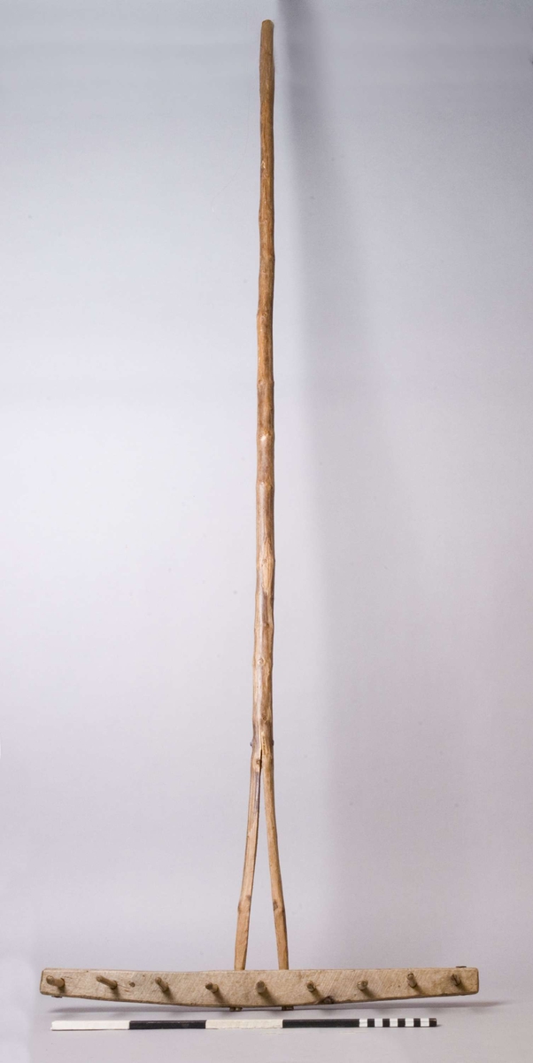 Räfsa, handgjord. Modell där nedre delen av handtaget, c:a 330 mm, är kluven och infattad i räfskammen. Förstärkt vid klovets början med genomgående spik och bricka. Även räfskammens ändar är förstärkta på samma vis. Nio pinnar, c:a 85 mm långa.