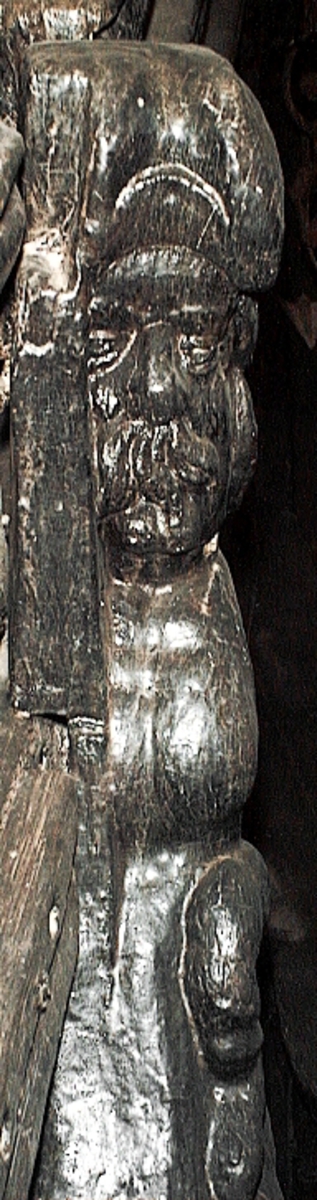 Skulptur av en triton, svängd mot höger.
Tritonen är framställd i vänster profil och avtecknar sig i hög relief mot det släta bakstycket. Tritonen har en stor näsa och treflikig mustasch. På huvudet sitter en hjälm med dekorativa bladvoluter. Armarna är ersatta av långa, flikiga bladslingor. Bålens övergång i den fjällförsedda fiskstjärten markeras av stora bladbildningar. Tritonens stjärt döljs bakom stjärten och vingen till en under liggande drake, se fyndnummer 21277. På baksidan finns urtag för relingslisten.
Skulpturen är mycket välbevarad.

Text in English: A sculpture of a Triton curved to the right.
The figure is seen in left profile, in high relief against a plain back board. The face has a large nose and a moustache that splits into three parts. On its head is a helmet with decorative leaf volutes. The arms are replaced by long, lobed leaf formations. The transition area between the male torso and the scaled fish-tail is decorated with large leaves. The rear is hidden behind a dragon''s coiled tail and broad wing situated below, see No. 21277. There are notches on the back that fit into the railing.
The sculpture is very well preserved.