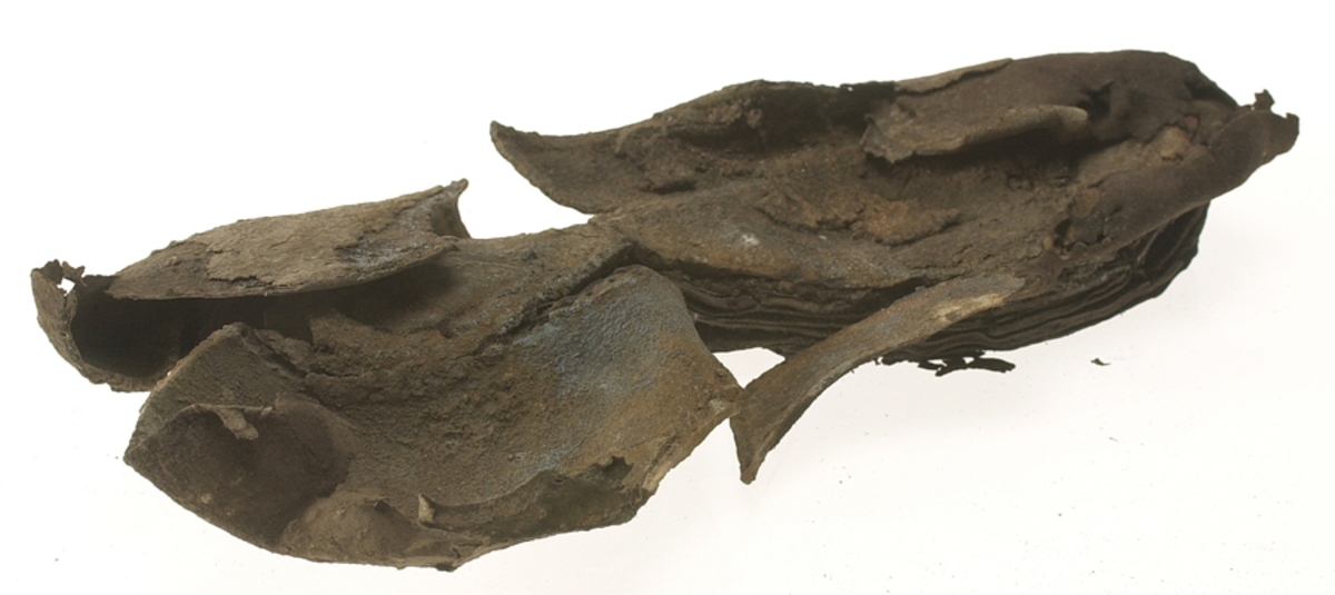 Sko.
Inuti skorna hittades även fragment från olika textilier som ursprungligen varit ett par strumpor. Idag sitter ett stickat fragment av ull fast i vänsterskon (23070) med avigsidan uppåt. I fyndet finns även en mängd lösa stickade fragment som idag är mycket korroderade och vissa helt mineraliserade av järn vilket har gjort textilen stenhård och därmed oerhört skör (23070a-c). Utifrån minskningar som några små fragment har så har det varit möjligt att rekonstruera strumpans tå. Genom att pussla ihop fragmenten som ursprungligen har suttit ihop har det på så vis gått att avgöra hur strumpans tå har varit konstruerad. Då textilen är så fragmentarisk är det inte möjligt att avgöra hur resten av strumpan har sett ut eller varit konstruerad. Däremot så finns det fragment av ett kypertvävt tyg av ull som på vissa ställen ligger dubbelt med det stickade 23070c). Ett av dessa fragment har stelnat i formen så som den suttit på fotens främre del inuti skon. Detta fragment täcker delvis det stickade tyget och har dessutom spår av kaststygn längs en kant. Så som det vävda tyget är placerat på det stickade tyget pekar på att man använt det som lagningslappar till sina stickade strumpor. 
I fyndet finns det även korroderade järnklumpar, ett tuskaftsvävt tyg av ull och rester av ett grovt bastfibergarn och två mindre läderfragment (23070d-f). Det är möjligt att även dessa har tillhört strumpan och/eller skon.

För mer detaljerad information från textildokumentationen (år 2022) se länkade filer.

Skodokumentation 2022:
Ovanläder. Tillverkad i getskinn av god kvalitet. Hör ihop med fyndnummer 23069 (Yngves skor). Tillverkades på en rak läst och bars på vänster fot. Inga dekorationer Det finns stygnhål som visar att det funnits invändiga förstärkningar (men förstärkningslappen saknas). Det finns delaminering men inga lagningar.
För mer information, se Länkade filer: Uppritning

Text in english:
This is the upper of a shoe of more “extreme fashion”, made of goatskin leather of good quality, probably made on a straight last and worn of the left foot, with no decorative features. The upper couples with 23069, together composing Yngve’s shoes. There are internal reinforcements missing from the upper and delamination, there are no repairs.
For more information, go to Länkade filer: Uppritning