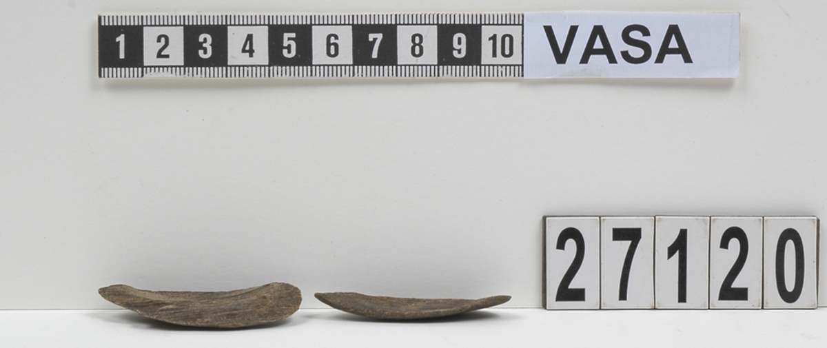 Två delar av en träsked. Delarna utgör mindre partier av skedbladet. På delarna syns en svagt rödbrun färg, vilket möjligen är spår efter bemålning.

Delarna är mycket slitna.

För mer information se Dokumentationsblankett under Referenser – Länkade filer.