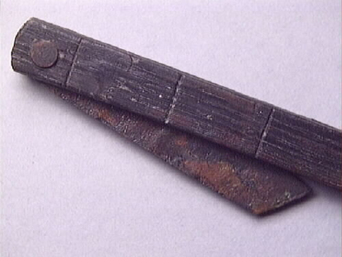 En vinkelhake, s k smygvinkel.

Skaftet är försett med sex stycken ristade skåror som markerar tum. I ena skaftänden sitter ett nytillverkat, ledat, järnblad. Bladet är fäst med en nytillverkad järnsplint. I skaftets ena ände, närmast bladet, löper en skåra eller ett spår. Spåret är mellan 68 och 80 mm djupt.

Smygvinkeln är i gott skick.

För mer information se Dokumentationsblankett under Referenser – Länkade filer.