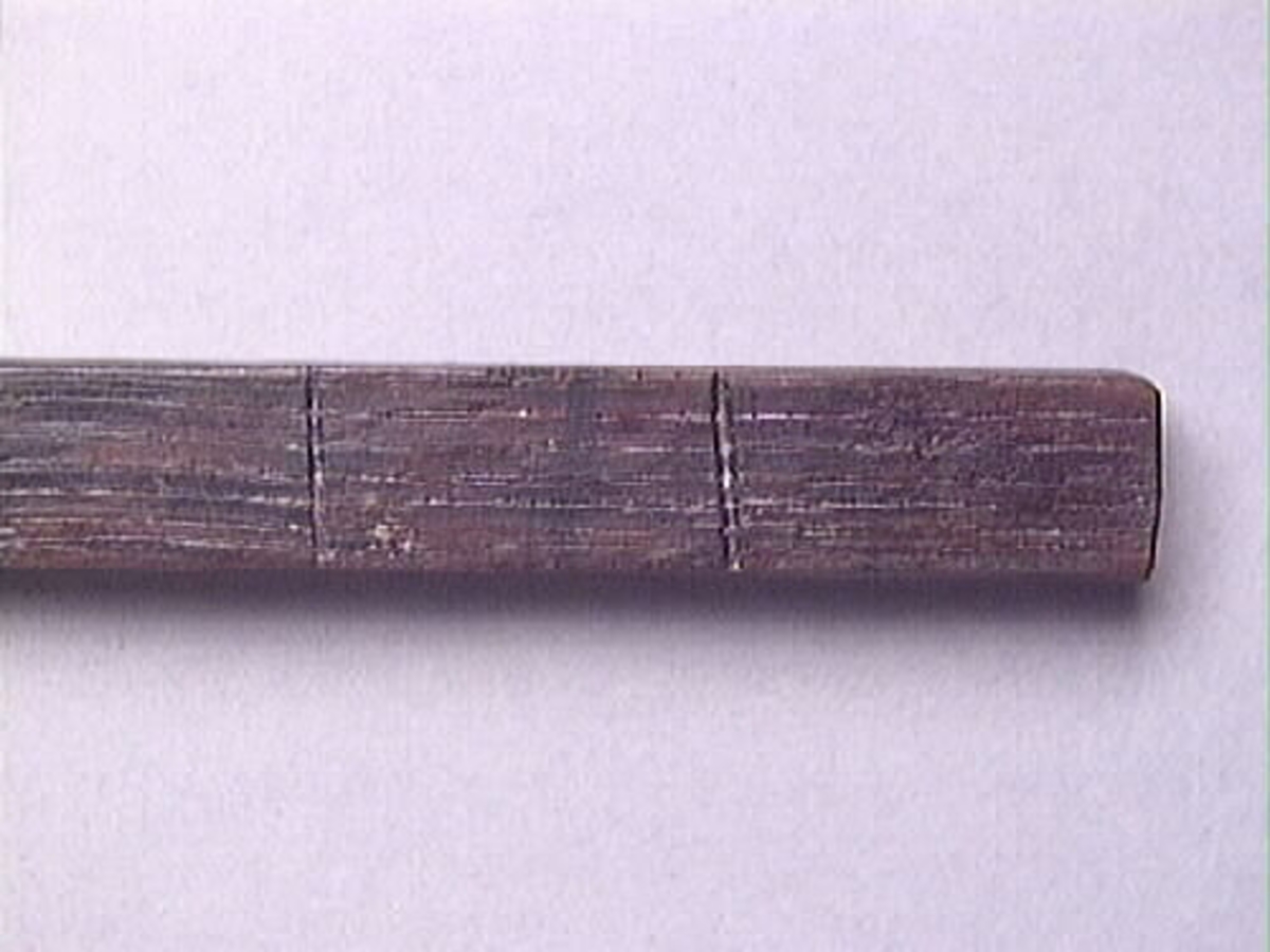 En vinkelhake, s k smygvinkel.

Skaftet är försett med sex stycken ristade skåror som markerar tum. I ena skaftänden sitter ett nytillverkat, ledat, järnblad. Bladet är fäst med en nytillverkad järnsplint. I skaftets ena ände, närmast bladet, löper en skåra eller ett spår. Spåret är mellan 68 och 80 mm djupt.

Smygvinkeln är i gott skick.

För mer information se Dokumentationsblankett under Referenser – Länkade filer.