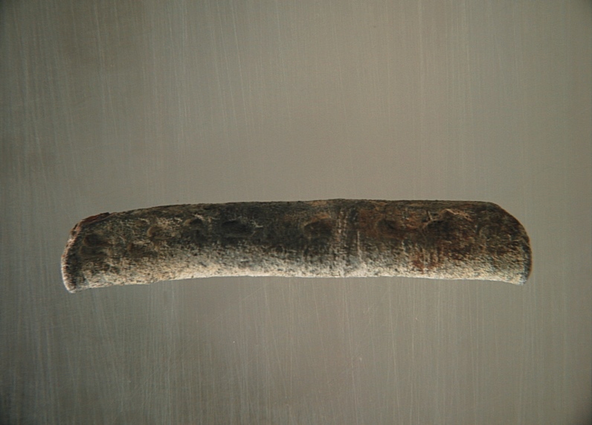 Sänket består av en vikt blybit. Sänket har tydliga märken efter det verktyg som pressat ihop sänket runt garntråden. Sänket är i gott skick.

Text in English: Lead sinker in the shape of a flat tube. The rectangular piece of lead is folded vertically in half and has visible tool marks from the folding process. The yarn is pushed through the hole. Grey mat in colour. In good condition.