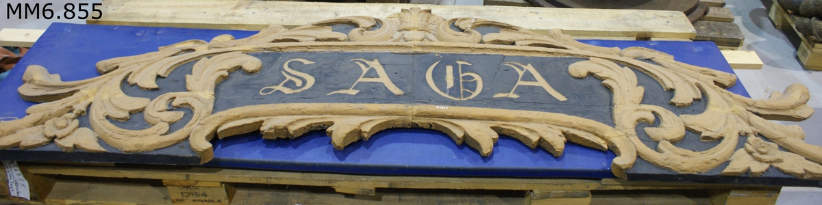 Akterstävsornament från ångkorvetten Saga (byggd vid Karlskrona örlogsvarv år 1878).

Av furuträ och utgöred av namnet Saga, omgivet av blad och blomrankor. Bottenfärg är svart, ornament och namn gula.