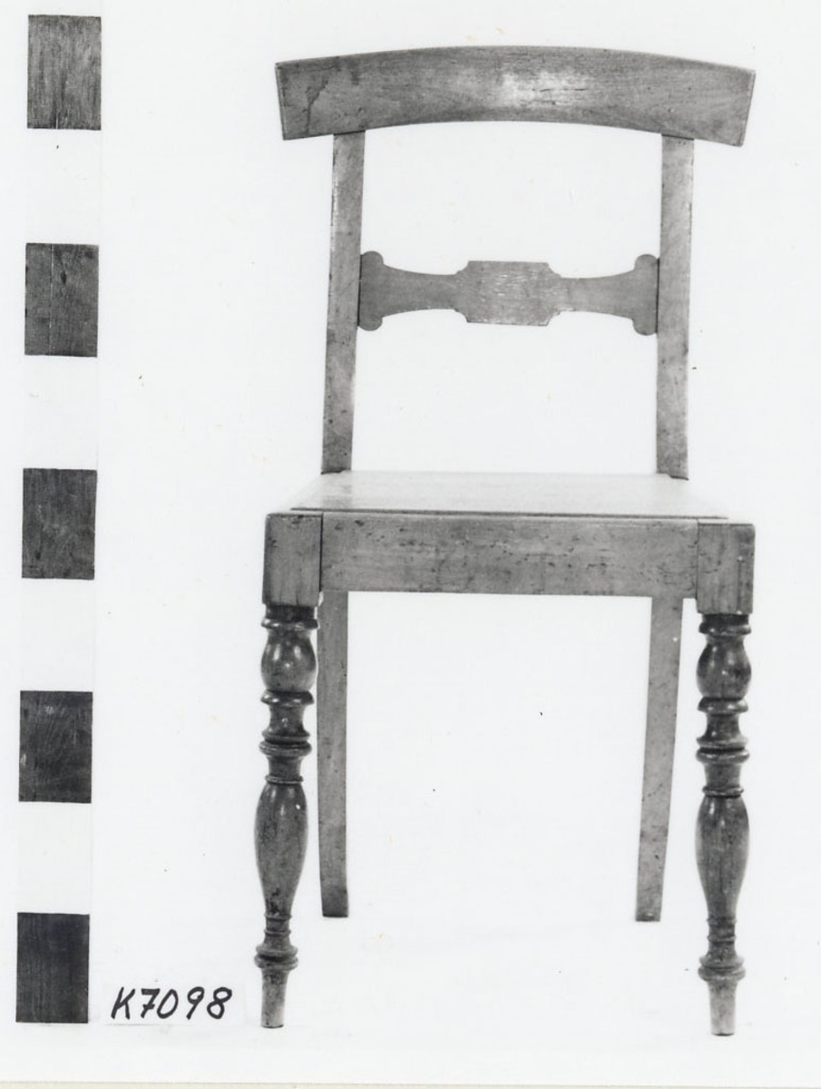 Stol av trä, fernissad. Svarvade framben och fyrsidiga, något baksvängda bakben. Rygg med kontursågad tvärslå samt slätt överstycke. Sitsen i ett stycke. Märkning i svart: "Corv. Najaden".