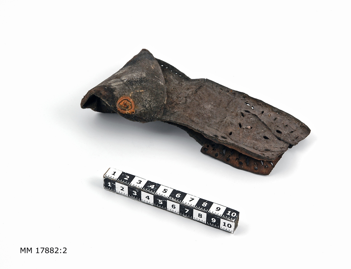 Sjöfynd från vraket Nya Riga. 16 fragment av läder, flertalet tydliga rester av skor med sula och klack försedd med pliggar. Spår efter sömmar. Hälften är större fragment.

För dimensioner på de enskilda bitarna, se inventariebilaga.