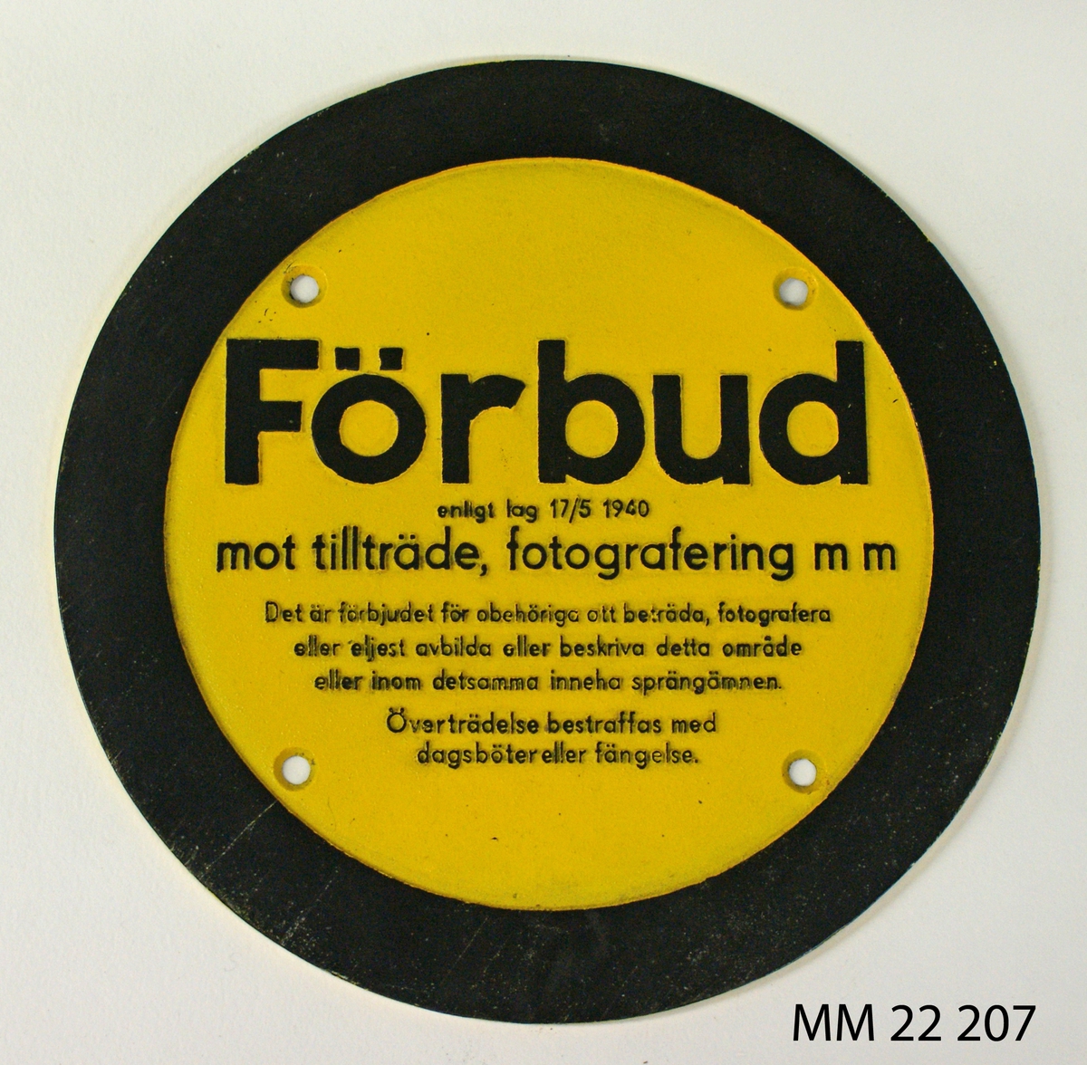 Skylt av aluminium gjuten, rund. Gul botten och svart text samt svart text och kant, bredd 25mm. Fyra hål för fastsättning.
Text: "Förbud mot tillträde fotografering..."