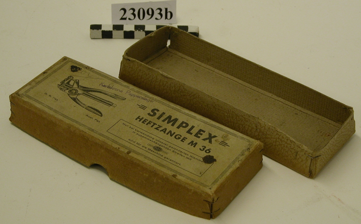 Papplåda med botten och lock av beigefärgad papp med mönstrad yta. Botten består av en pappbit i vilken kvadrater i hörnen klipps bort, kanterna vikts upp och hörnen häftats ihop med häftapparat. På locket en klistrad lapp med en tryckt bild av häftapparaten och text "SIMPLEX HEFTZANGE M 36 D.R. Pat. Ausl.Pat." Inom ram står texten"Nur bei Verwendung unserer patentierten Klammern in zusammenhängenden Streifen mit SCHUTZ ELA STIC MARKE wird für die Maschine garantiert." Med violett stämpel står "Karlskrona Papperslager". Med blyerts står i övre vänstra hörnet ett oläsligt ord i skrivstil.