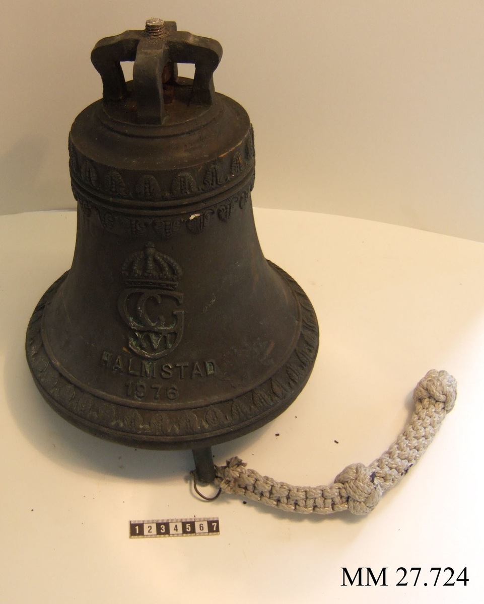 Gjuten skeppsklockan av kyrklocksmodell. Märkt med Karl XVI Gustafs namnchiffer samt texten Halmstad 1976. Kläpp i klockan med  längden 250mm.