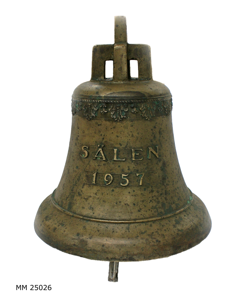 Skeppsklocka av brons. Märkt i relief "Sälen 1957". Ornamentslinga i relief längs toppen. Kläpp av svartmålat stål och brons. Klockan något ärgad.