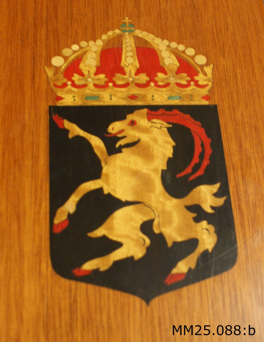 Rektangulär trälåda i mörkt fernissat trä. Lådan är försedd med lock och lås. På lådans lock finns en målad vapensköld med en get som står på bakbenen. Vapnet försett med krona. Längre ner sitter en metallskylt med två korsade flaggor, flankerade av två vapensköldar, samt text "Jagaren Hälsingland 1959" ingraverat.