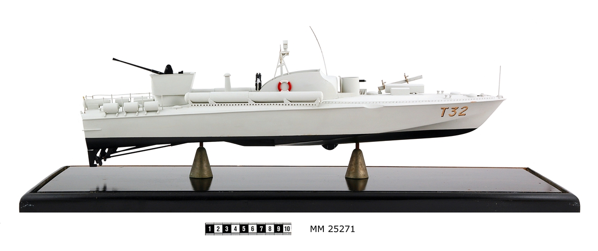 Modell av motortorpedbåten T 32. Från vattenlinjen och neråt målad i svart, från vattenlinjen och uppåt målad i ljusgrått. Märkt på stäven med skuggade bokstäver i guldfärg: "T32". På fördäck står en lysraketkastare och i en upphöjd brunnskonstruktion en dubbel KSP M/36. Mitt på fartyget en brygga med styrratt. På var sida om och bryggans sköldliknande upphöjning sitter en röd och vit frälsarkrans och något akter om dessa dubbellavettage med kulspruta M/36. Akter om bryggan sitter en luftvärnskanon i ett upphöjt brunnslavettage.
Modellen sitter på två konliknande fästen i en glasmonter med svart botten. Dimensioner avser modellen.