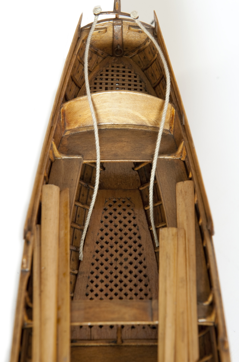 Gigg, bordlagd på spant, klink med fullständig inredning. 6 årtullar, 6 åror. Roder med skädda. Fernissad, Stativ fernissat. Masten saknas.