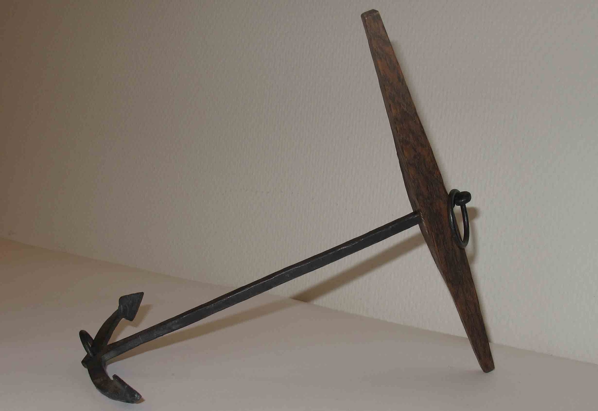 Modell av stockankare av järn med fyrkantig lägg, platta armar, små trapetsformade flyn (elsvetsade). Liten ring i kronan. Stock av ek med liten påspikad kloss.
