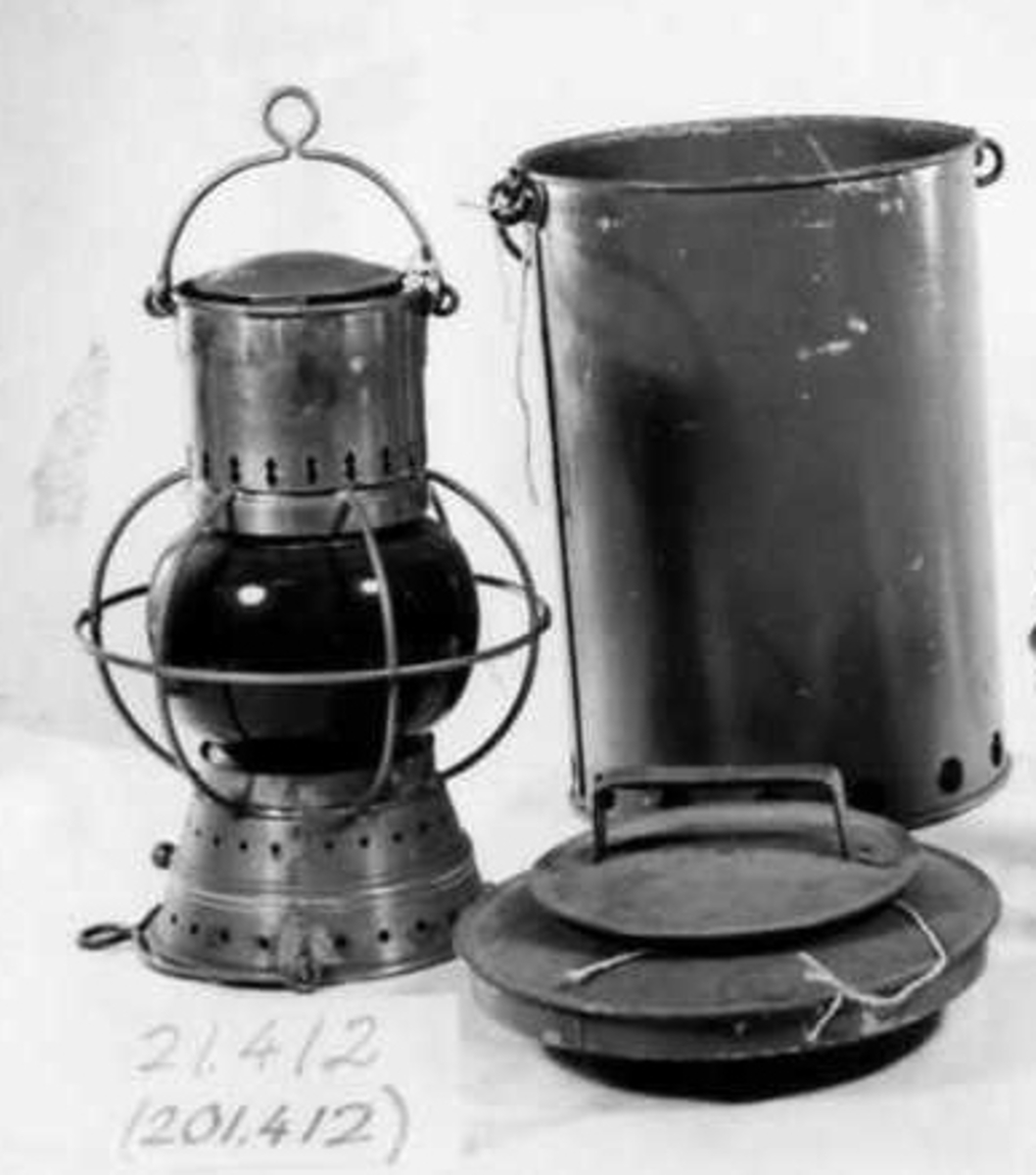 Cylindrisk behållare med ventilhålskrans nedtill, grepe, lock med tre fjädrar som griper runt huven och ventilhål, lanternfot stympad kon med ventilhål, sfäriskt glas med mässingsgaller, cylindriskt rökfång med grepe, grepe nedtill, stympad kon som fotogenbehållare med två porslinsplattbrännare insätts via botten.