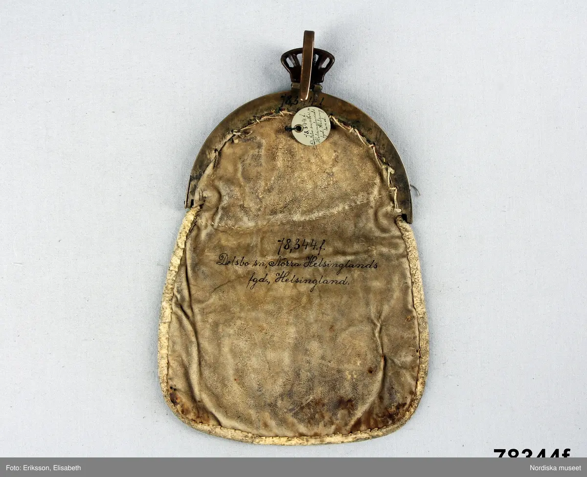 Huvudliggaren:
"Kvinnodräkt fr. Delsbo sn, Norra Helsinglands fgd, Helsingland.
a. "Ryntjeskjortel" af svart kläde med röd kant och bandväfd "kval" (linning). Kjolen "lurad"(goffrerad), skall förvaras lurad att ej vecken gå ut. 3 par fruntimmershänder hjälpas åt att "lura" den efter hvarje begagnande.
b. livstycke, rött med gröna ränder.
c. "Ryntjessärk" (rynksärk) af hvitt bomullstyg med "krus" (handbroderi) kring hals och händer.Begagnas sommartiden
d. "Bumsförkläde" af ylle, blårandigt med bandväf,"kval" i rödt och grönt.
e. "Förklesband" rödt och grönt ylle med "doppar" (tofsar) i ändarna. Lindas 1 à 2 hvarf kring lifvet och bindes framtill med stora nedhängande "locor" och ändar. Längd 262 cm, bredd 3,4 cm.
f. Kjolsäck med mässingslås och hake samt tennbroderi. Häktas under förklesbandet och hänger delvis under "försklet". Begagnas vanligen till förvaring af kyrkkryddor m.fl. kyrk-ellerkalassaker.
g. Halfhandskar af svart kläde med silkesbroderi. Begagnas sommartiden.
h. "Påshufva" hvardagsmössa af brokigt kattun. Begagnas med i nacken utslaget hår med några hårtestar hängande fritt framför öronen.
Till dräkten användes röda strumpor samt låga skor med höga klackar. Äfven kan användas silfersmycken kring halsen eller å  bröstet. En á två brokiga silkesdukar brukades omkring halsen nedstoppade under lifstycket, så att kruset kring halsen  på "ryntjessärken" sammanfästadt med ett löfspänne samt en smalare kant af hvarje sidenduk, blevo synliga. Vid handlederna sammanfästes ryntjessärken med röda sidenband eller länkknappar.

a. KJOL 
längd: 87 cm
midjeband bredd: 7 cm
av svart halvylle med svart linvarp och inslag av svart 1-tr. ullgarn, de 2 yttersta stadtrådarna är av oblekt lingarn. 4 goffrerade våder samt en slät framvåd som skarvats under förklädet med oblekt bomullslärft. 5 cm bred list av rött kläde i nederkanten runtom. Brett midjeband mönstervävt i rött och grönt ullgarn och vitt bomullsgarn. Knäppt vid framvådens vänstra sida med 2 hakar och hyskor av mässing.
b. LIVSTYCKE
längd: 39 cm
av halvylle i varptäckande kypert, varp av vitt lingarn, inslag av svart och grönt ullgarn med flaminslag av vitt, 2 fram-och sidstycken, 2 bakstycken avsmalnande till skörtveck med tre par tränsade förstärkningar av svart garn. I midjehöjd ett avsytt veck runtom, knäppt kant i kant med 8 par grova hakar och hyskor av mässing. Foder av ofärgad bomullslärft.
BE

c. ÖVERDEL
Längd: 39 cm. Längd: 58 cm - ärmlängd. Vidd: 56 cm - ärmvidd. Vidd: 114 cm. Höjd: 1,7 cm - kraghöjd. Material: Textil, bomull. Textil, linne - ärmlinning, krage. Bomullsgarn - broderi. Telnik: Tuskaft. Trådbundet broderi. Broderi, rätlinjig plattsöm. Handsömnad.
Överdel av tuskaftat vitt bomullstyg. Dubbelvikt bålstycke, isydda rektangulära halsspjäll. Täta breda stripade  rynkor mot halskrage i bomull, 1,7 cm hög. Kragen har broderier i rätlinjig plattsöm, vitt bomullsgarn över hela ytan, nuggor i kanten, langetterade bågar  i framkant. 16 cm långt sprund fram, tränsad förstärkning nedtill, 3 cm.  Vidsydd ärm med  infällda ärmspjäll, lagda veck över axeln fram och bak. Täta breda stripade rynkor mot 2,5 cm bred ärmlinning. Ärmlinningen har yttäckande vita broderier i rätlinjig plattsöm, rombiska former. Vita knytband i bomull i ärmlinningar och krage. Överdelen är handsydd.
/Inga-Lill Eliasson 2007-11-26


d. FÖRKLÄDE
längd=vådbredd: 82 cm
bredd: 97,5 cm
av halvylle, varp av svart lingarn, inslag i varptäckande kypert av svart 1-tr. ullgarn med smala ränder istarkt blått och en knappt synlig svart tråd med vita flamgarnsfläckar av bomull. Upptill stripade rynkor där de blå bårderna utnyttjats dekorativt i rynkningen. Mönstervävt midjeband i grönt på rött ullgarn , bandet knäpps med 2 hakar och hyskor i vänster sida.
I nederkantens båda hörn infodringar på insidan av svart bomullslärft, för att tyget inte skall rulla sig.



Berit Eldvik 2004