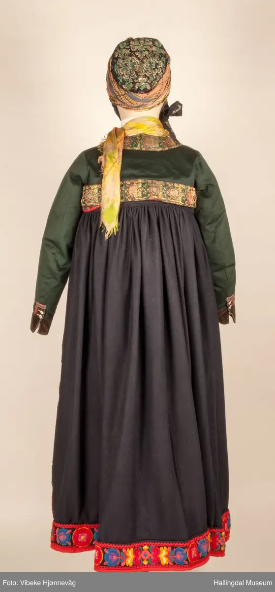 Kone fra Nedre Hallingdal i hallingbunad.  Kona står utstilt i den faste bunadutstillingen på Hallingdal Museum, Nesbyen.  Hallingbunaden består av mange draktdeler; trøya HFN 01835, Forkle HFN 03381, stakk, liv, lue, silketørkle rundt lua, silketørkle rundt halsen HFN 03500, bringduk og skjorte.