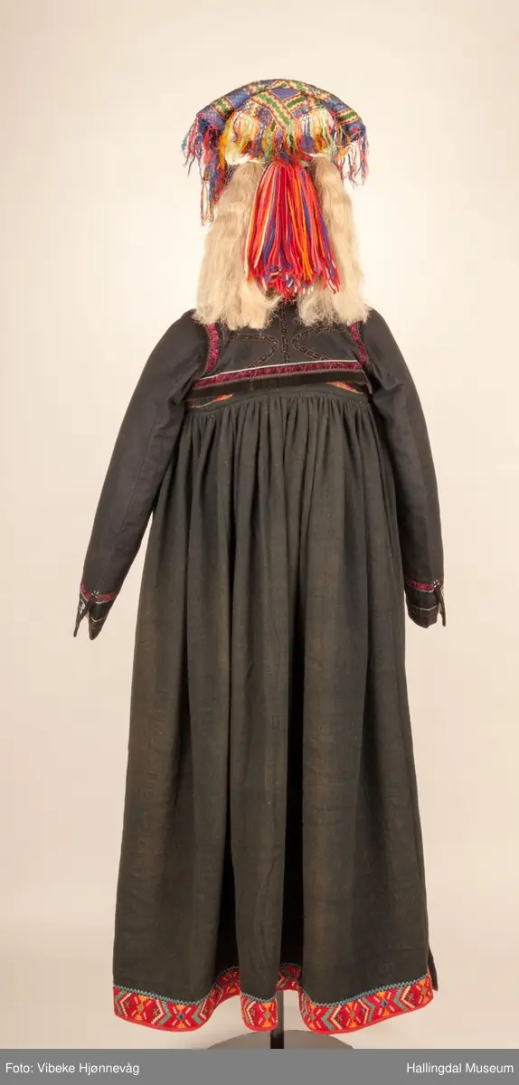 Kone fra Øvre Hallingdal i hallingbunad.  Hun bærer hette.  Kona står utstilt i den faste bunadutstillingen på Hallingdal Museum, Nesbyen.  Hallingbunaden består av mange draktdeler; trøye, Forkle HFN 02033, stakk, hette, silketørkle i halsen, perlet bringduk el. brystklut og skjorte.