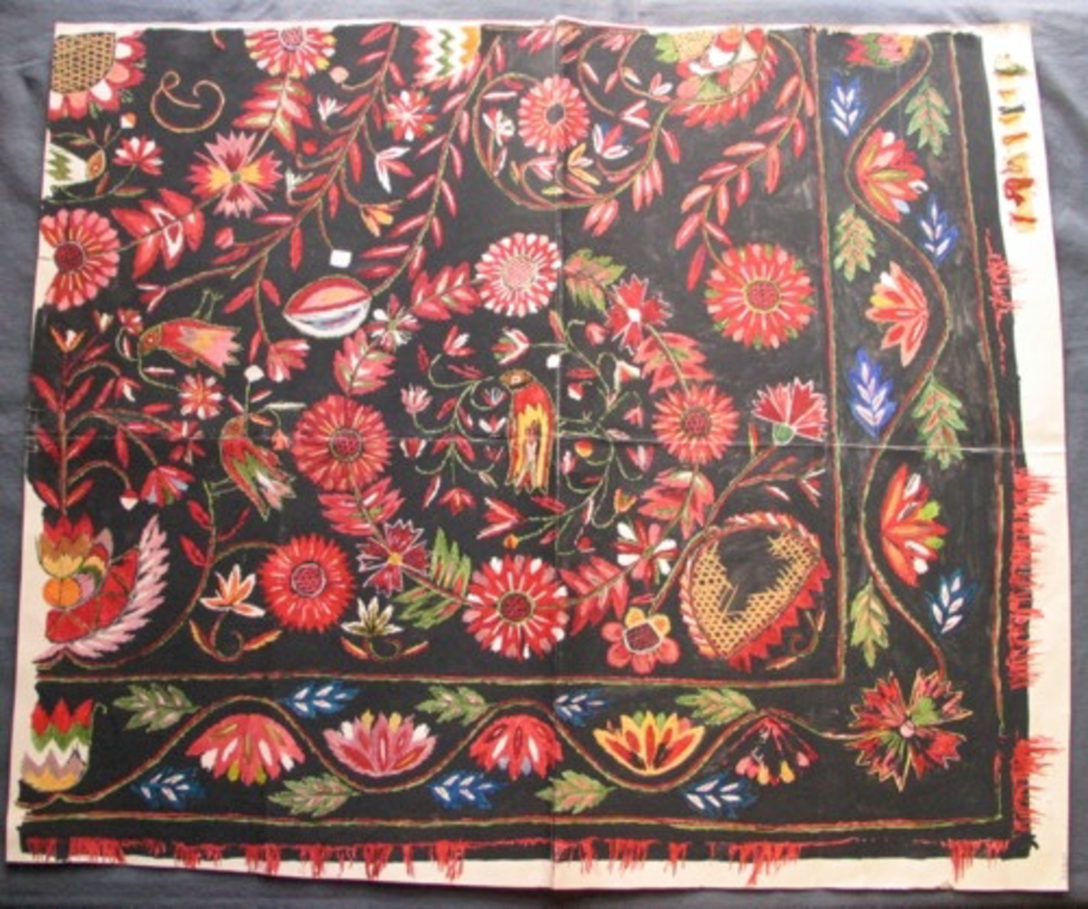 Skiss målad på styvt papper. Skiss på del av täcke på svart botten. Bred bård, ca 150 mm, med eklöv och blommor. Stor blomcirkel i mitten med monogram och fåglar. I hörnet en blomcirkel med fågel, 390mm. Utfyllnad med blomrankor och fåglar. Röd kavelfrans längs kanterna. Flera röda nyanser, gult, blått, vitt och grönt. I ena hörnet fasttejpade garnprover.