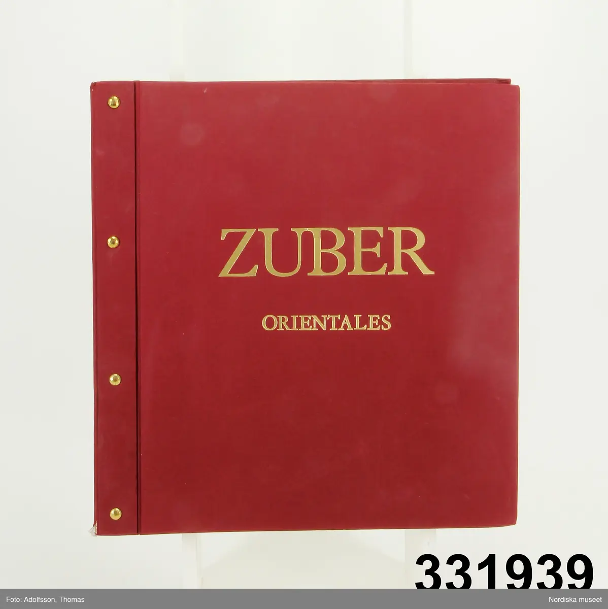 Tapetprovbok med vinröd pärm. På pärmens utsida, text i guld: "ZUBER ORIENTALES". På försättsbladet: "ZUBER & CIE Impression à la main de papiers et tissus de Haute Décoration. Rixheim-Alsace- France. Depuis 1797".

Provboken innehåller prover på handtryckta papperstapeter, tapetbårder och gardintyger i orientalisk stil i klara starka färger. Bottnar i rött, svart, grönt, mörkblått, figurativa mönster med asiatiska män och jaktmotiv med turbanklädda jägare med sablar och pilbågar. Det flesta tapeterna har täta vegetativa mönster med blommor, blad och fåglar. 

På  pärmens insida prislista över tapeterna i "Kollektion Oriental" från 1988. Där framgår att mönstren kallas Assam, Chasse persanne, Chekou, Mandarin, Chale indien, Dauphins, Florival, Moriviller och Bahamas. Priset på tapeterna var 1988 391-424 kr/rulle exklusive moms.
/Maria Maxén 2013-05-25