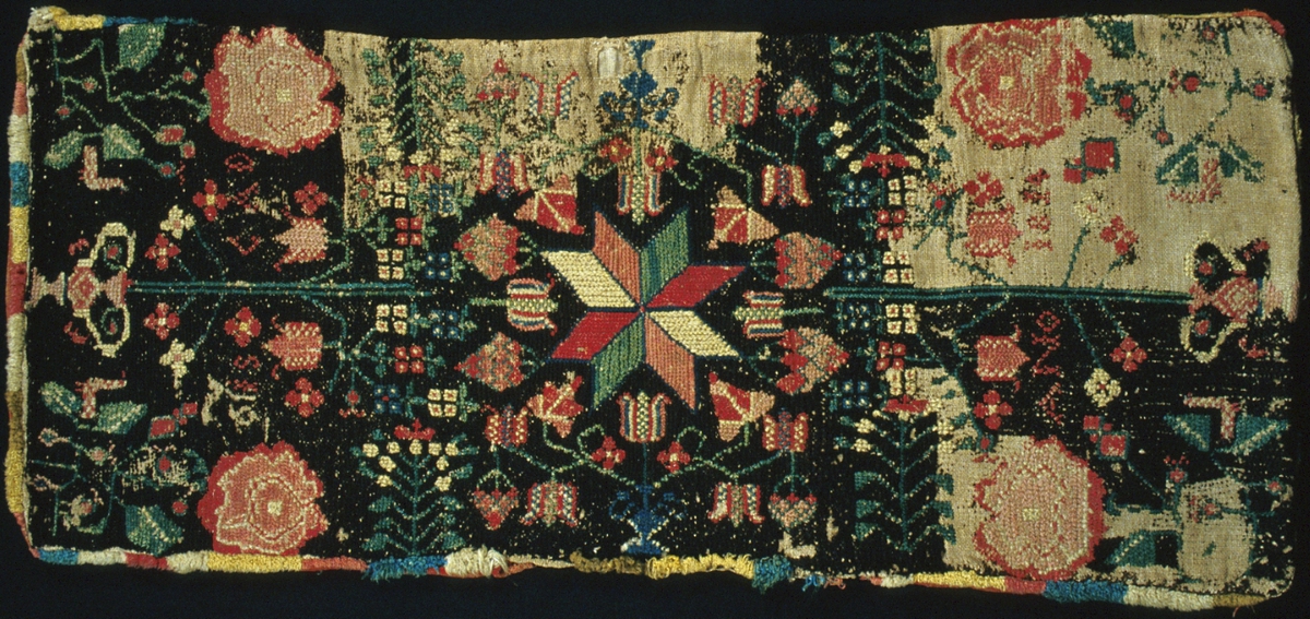 Åkdyna broderad i tvistsöm och korsstygn. I mitten en spetsuddig stjärna med åtta skarpt markerade vingfält. Urnor med blommor. I varje hörn en stor ros. Svartbrun botten med mönster i vitgult, två nyanser grönt, tre nyanser rött, rosa och blått. Broderad märkning i röda korsstygn: "ANO 1814  OIS CAD". Runt om längs kanten en frans liknande kavelfrans i gult, rött, blått, vitt och grönt ullgarn. Linnebotten vävd i panama. Brodergarn i 1-trådigt ullgarn, sydd med två trådar tillsammans.  Botten och de flesta mönster är sydda i tvistsöm, enstaka stygn, diagonala linjer och konturer är sydda i korsstygn. Bottengarnet är bortslitet på stora partier. Åkdynan har spår av fjäder inuti. Baksida i rött ylle, vävt i tuskaft och skarvat med bitar vävda i kypert. En 270 mm lång öppning i ena långsidan.Märkt med tygetikett på baksidan med texten: "A. N° 111  Landstinget". Mönstret finns i flera varianter, bland annat på Kulturhistorisk museet i Lund.
