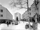 Hökarängens centrum
Exteriör, i bakgrunden, flerbostadshus med butiker i förgrunden. Barn, bilar, vinter.