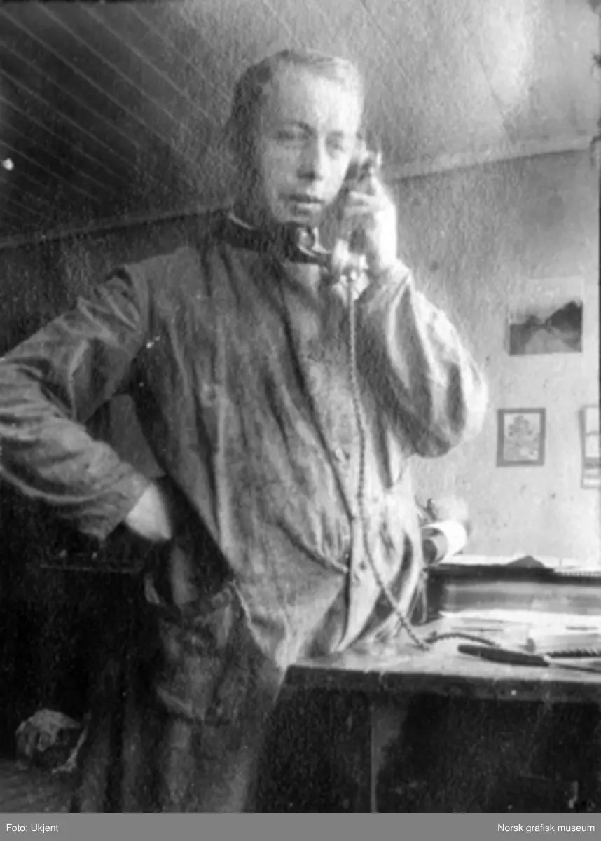 En ung mann i arbeidsklær står og snakker i telefonen.
Albumtekst:
"Javel!!! Nei han e ute (kan ikke si hvor)
1919"