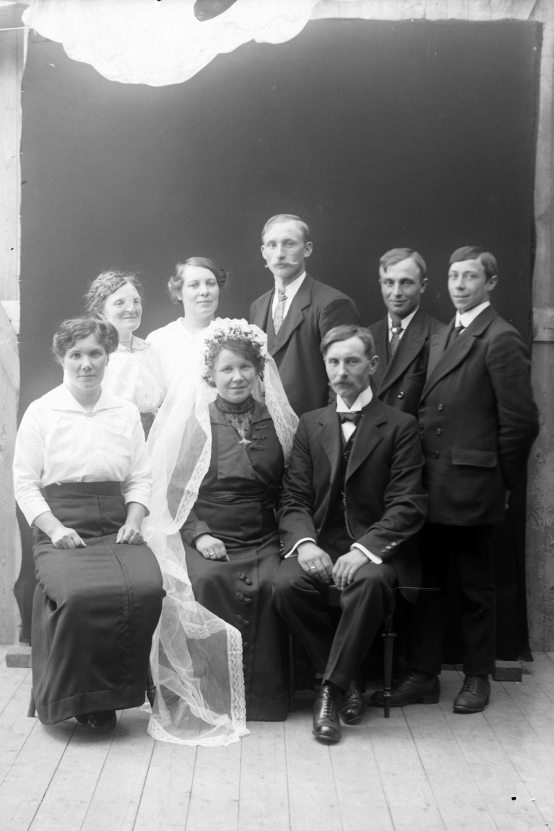 Gruppeportrett tatt i studio av et brudepar med familie og forlovere.