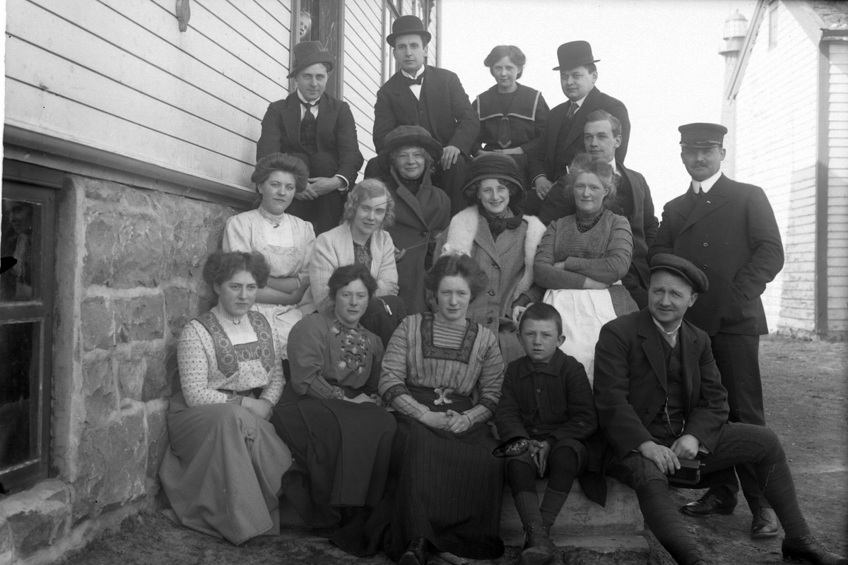 Gruppebilde av menn og kvinner på en trapp, med Andenes fyr i bakgrunnen.