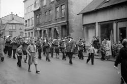 Skolekorps marsjerer ned Strandgata. I forgrunnen et par små