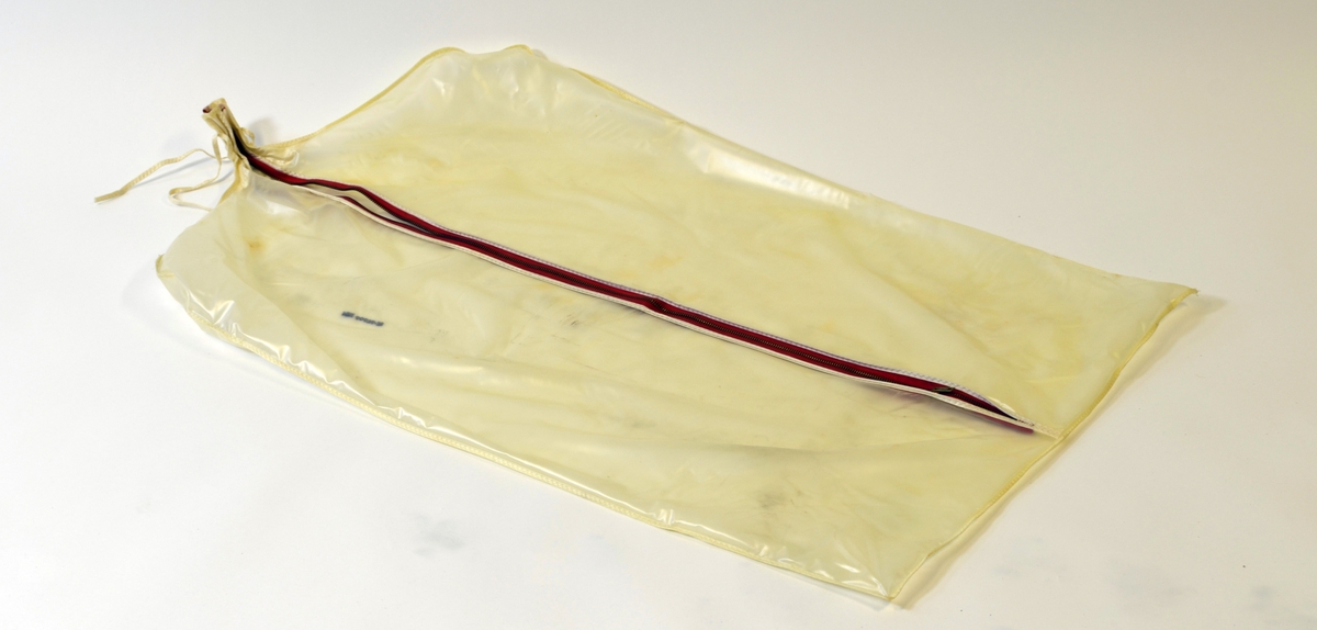 Gjenomsiktig klespose med glidelås i lengden og bendelbånd til å knytte sammen rundt kleshengeråpning. 

Posen er brukt til oppbevaring av ullpleddene som er registrert under MBI.00076-MBI.00078.