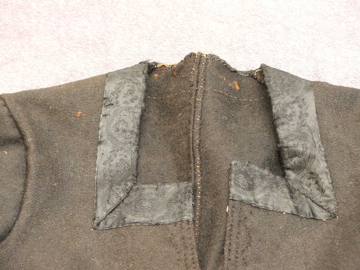 Svart blomstra silkeaktig band på
kragen. Rette og bølgeforma prydsaum på kvar side av opningen framme.