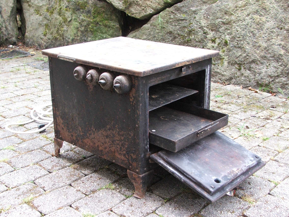 Elektrisk steikjeomn. Dør på eine kortsida med lukkemekanisme øvst. Tjukke veggar. Inni er det to lause steikjeplater. Det er spor til å setje plater på på veggane. Ei plate har kant, den andre ikkje. Øvst på eine langsida er det fire brytarar. Ledning kjem ut på kortsida bak.