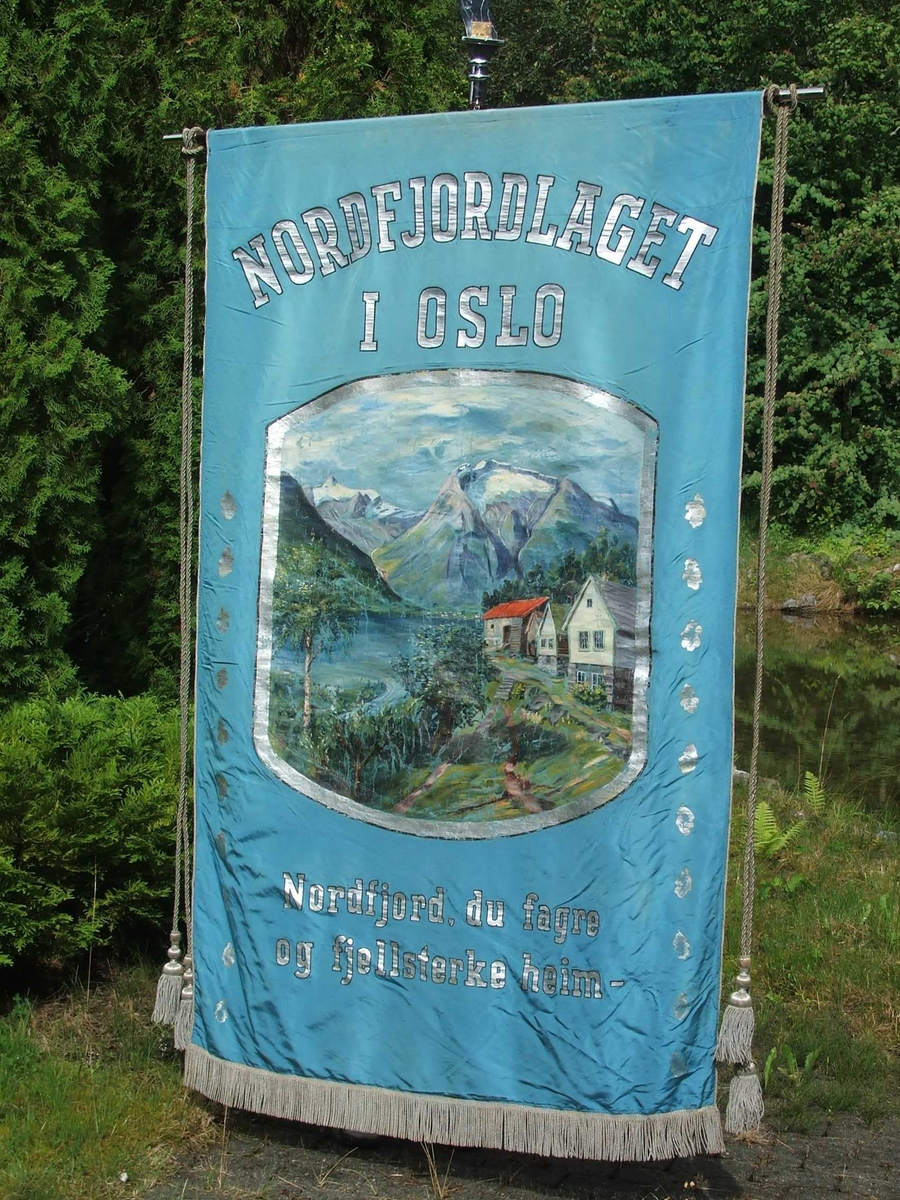 Gardstun med fjord, fjell og bre i bakgrunnen på framsida. På baksida skal det vere Holvikejekta som er måla i ein enkel strek. Tekst på framsida er "Nordfjordlaget i Oslo" over måleriet. Under "Nordfjord, du fagre og fjellsterke heim". 10 blader i rad på kvar side av motivet. 