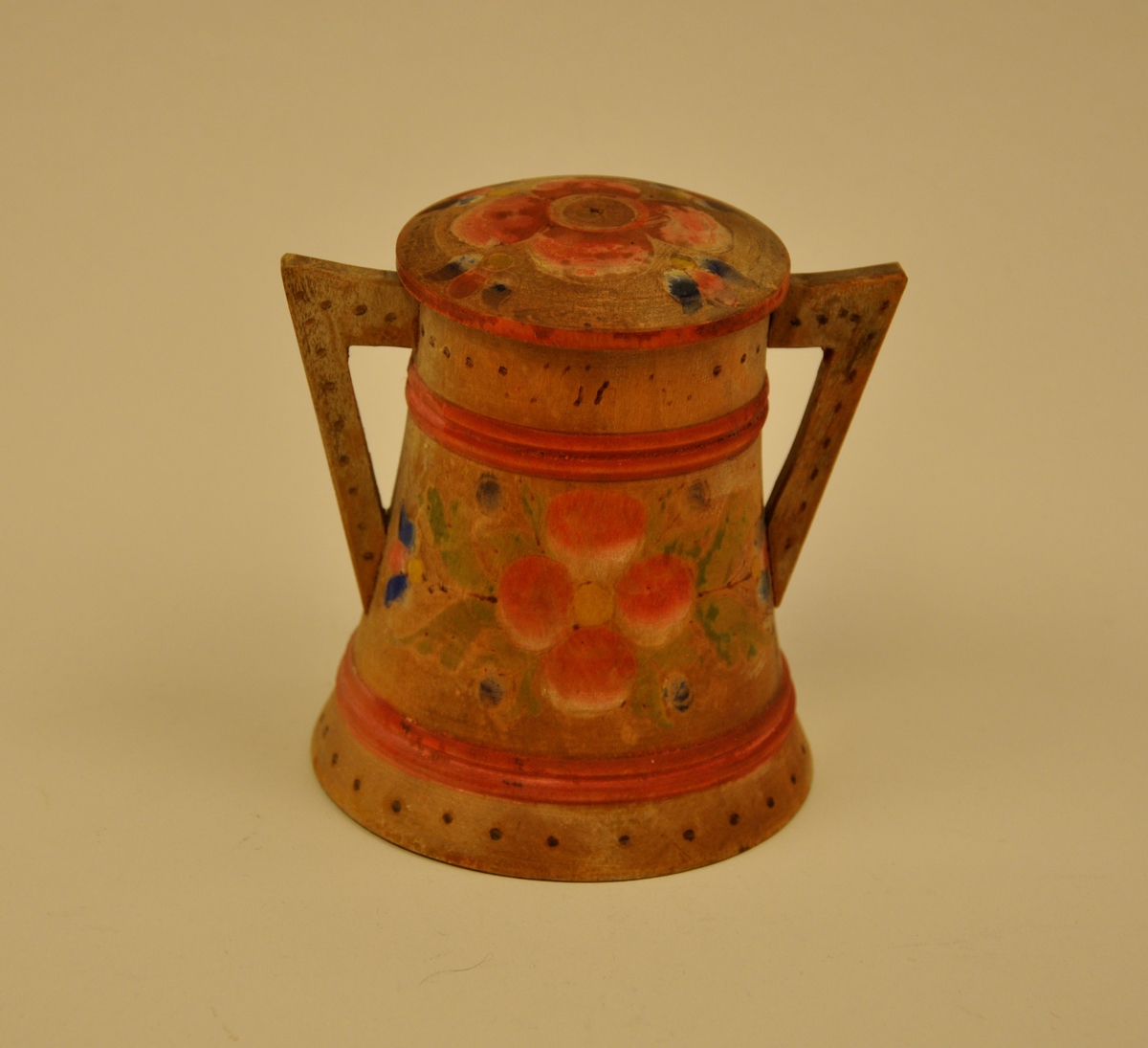 Begeret er breidast nede og smalnar jamt av oppover til kanten. Det har ei klar tredeling som kjem av stripene som skal forestille vidjeband. Dei tre felta har ulik dekor; det underste har ein ring rundt med svidde prikkar, det midterste har det norske våpenskjoldet på eine sida og ein slags rosemåling på den andre sida og det øverste har ein ring rundt med prikkar og innskrift. Hankene er nesten rettvinkla og dekorert med svidde prikkar. Loket er lett bua og har lik rosemålingsdekor med raud rose som midtpartiet