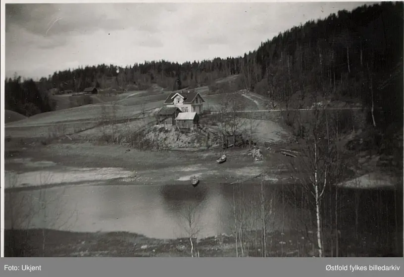 Grytheevja, Ovaskog. Bildet er tatt fra Grythebrua, som ble revet i 1939. Huset tilhørte Marius Lunde F.1889, far til eier av bildet, Mina.

Gunnar Kullerud skriver i 2013: 
Bildet kan ikke være tatt fra Grytebrua, den lå 70-80 m lenger inne i Gryteevja. Vi kan se at bildet er tatt fra land og det er helt sikkert at fotografen har stått på plassen Fauli, tilhørende gården Kongsrud i Ovaskog i Varteig. Det hvite huset heter fra gammelt av Betania.