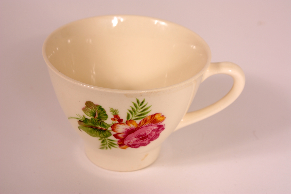 Fiolett blomster m/grøne blad, ein stor på venstre og ein mindre på høgre sida av hanken.