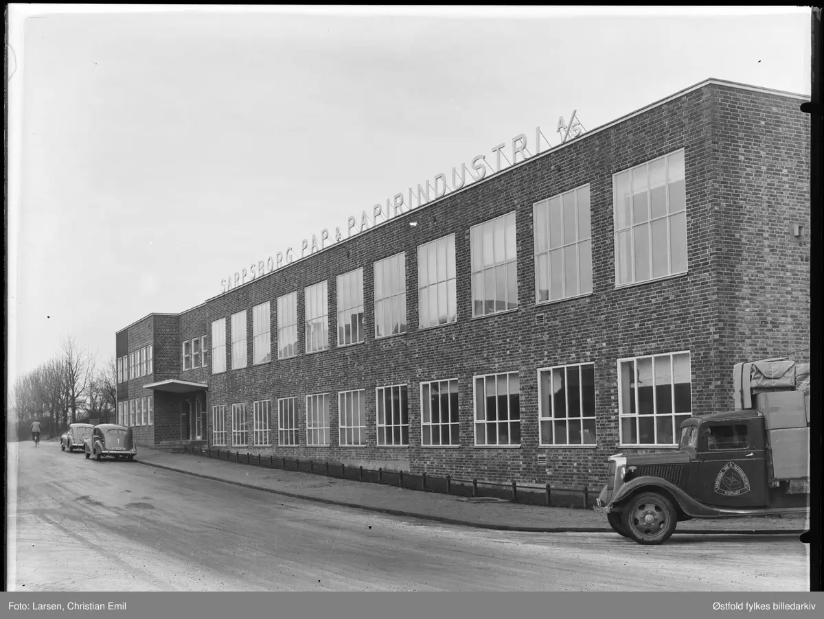 Sarpsborg Pap og Papirindustri A/S i Sarpsborg, eksteriør bygning i mur. Bygning oppført 1937 og tegnet av arkitekt Arne Pedersen.
To personbiler, A-20688, lastebil med firmalogo, ikke synlig kjennetegn.
Ford V8 lastebil årsmodell 1936, kfr. emblem rett over/bak lykta. Norskbygd førerhus. Forkrommet radiatorkappe var ikke standard.